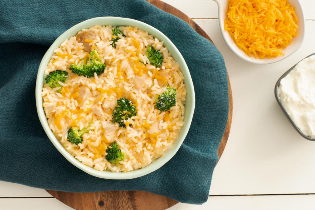 A bowl of white rice topped with broccoli, chicken and melted cheese